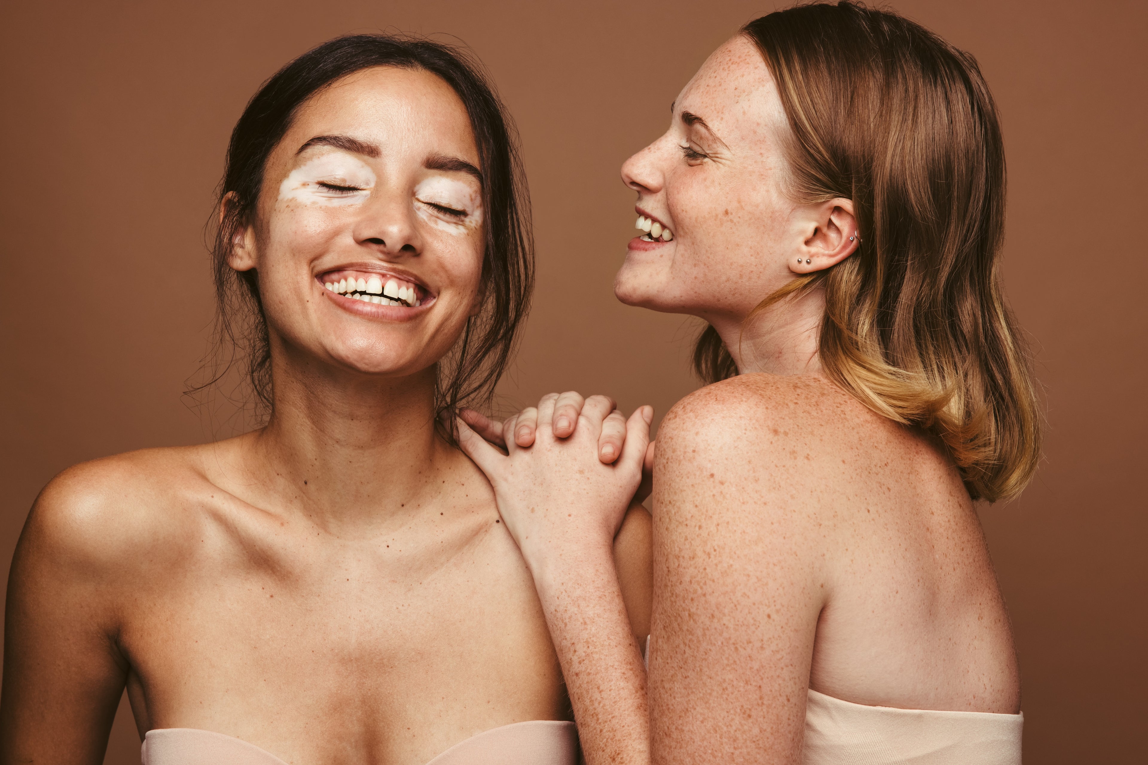 Two women with bare shoulders against a brown background