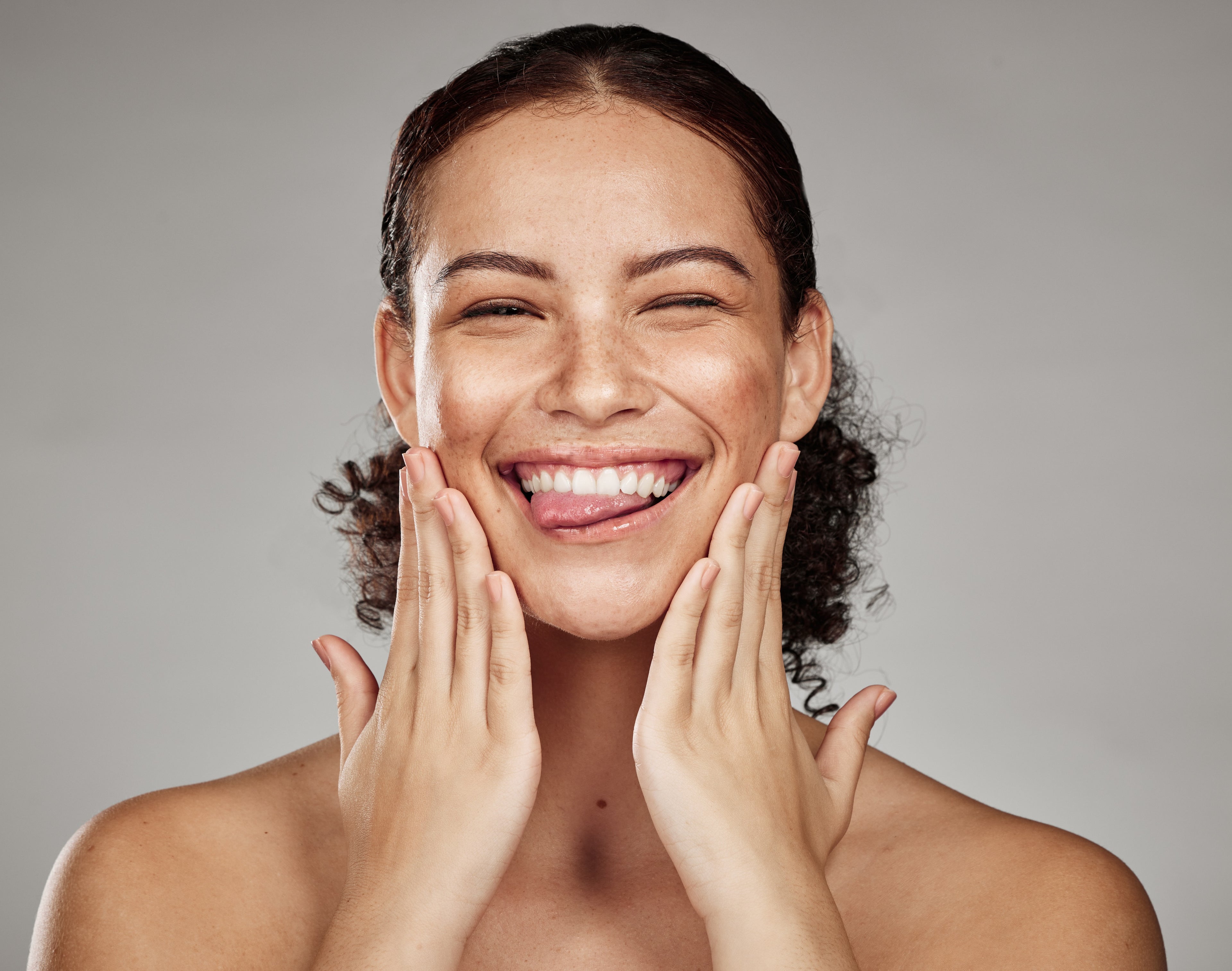 Woman with a radiant smile touching her face against a gray background