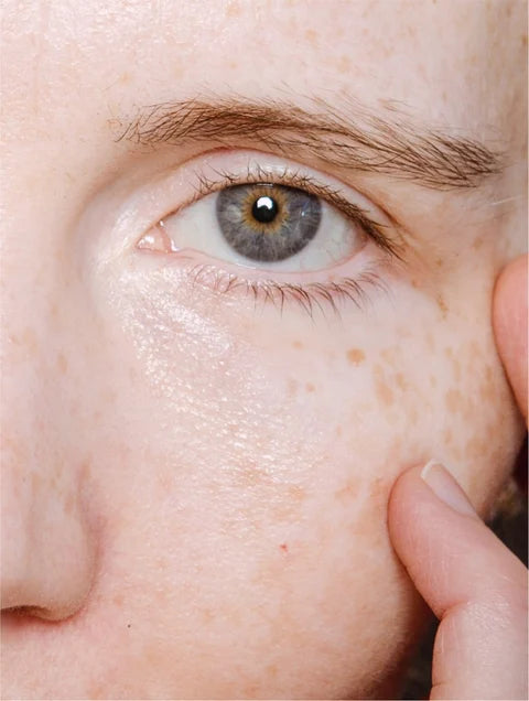 Close-up of a person's eye with a finger touching the skin around it.