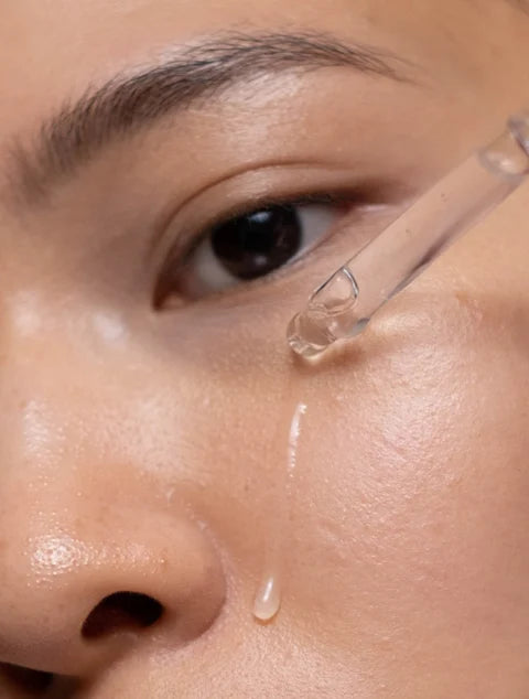 Close-up of a person applying a dropper of liquid to their skin.