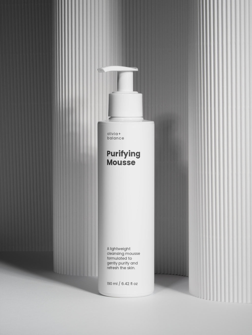 White bottle of 'Purifying Mousse' with a pump on a gray background