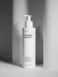 White bottle of 'Purifying Mousse' with a pump on a gray background