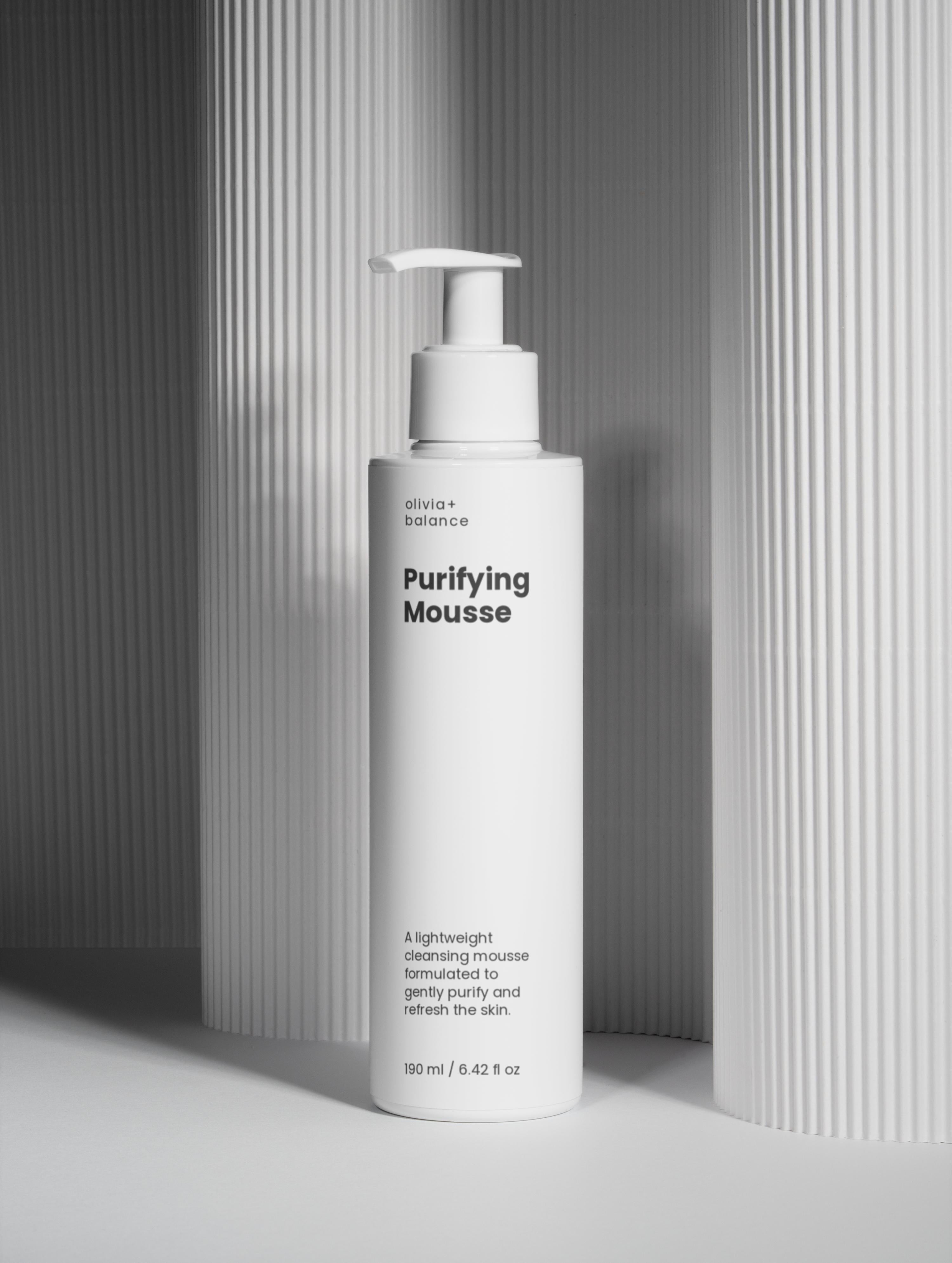 White bottle of 'Purifying Mousse' with a pump on a gray background